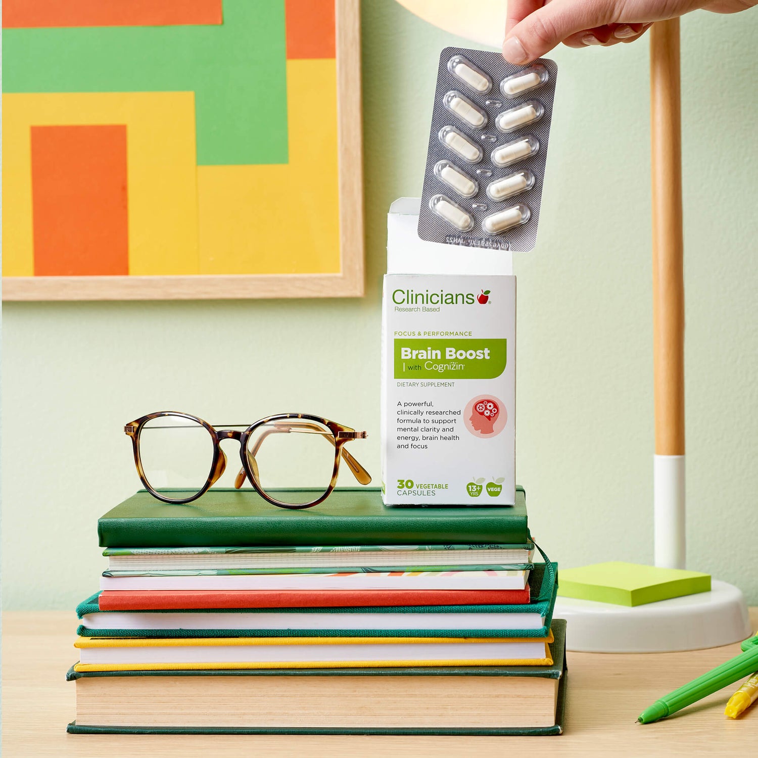 Capsule product on stack of books with reading glasses